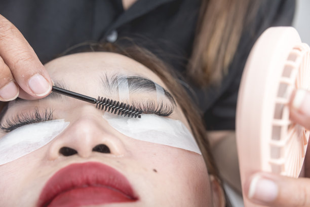 一位美容师一边用睫毛辊为顾客的睫毛定型，一边拿着扇子加快固化速度。图片下载
