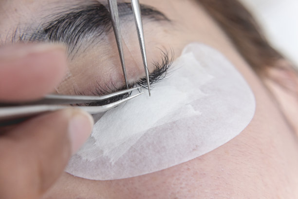 一名美容师准备在一名亚洲女性的睫毛线上插入一个单独的睫毛。图片下载