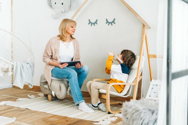 一个白人学校的男孩在他妈妈用平板电脑上网的时候给她拍照。学龄前儿童在玩相机图片下载