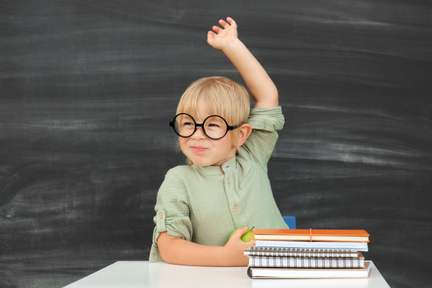 回到学校。快乐微笑的小学生戴着圆眼镜坐在课桌前。教室里有个孩子在黑板上举手。小男孩，上小学的。秋天的第一天。图片下载