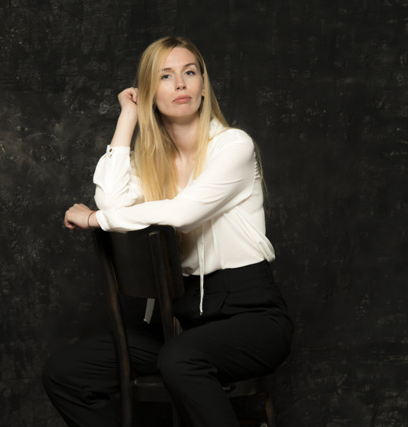 一个美丽的金发女人的肖像，一头长发，白色衬衫和黑色裤子在灰色孤立的背景。一个迷人的女孩在黑暗的背景上摆姿势。图片下载