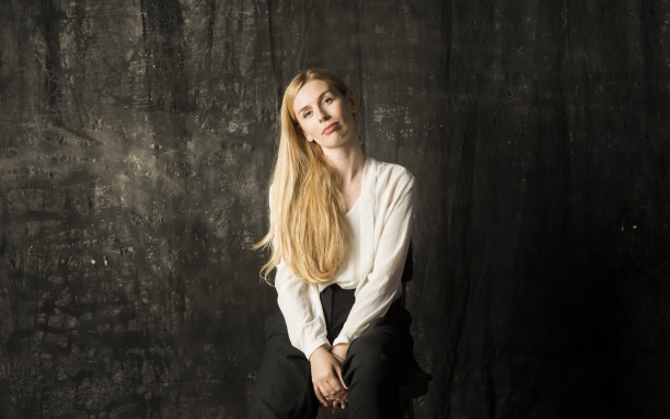 一个美丽的金发女人的肖像，一头长发，白色衬衫和黑色裤子在灰色孤立的背景。一个迷人的女孩在黑暗的背景上摆姿势。图片下载
