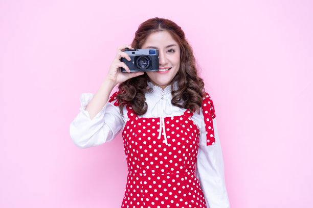 一个年轻微笑的亚洲女人的肖像在红色连衣裙拍照的复古相机孤立在粉红色的背景图片下载