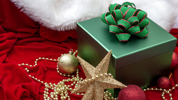 圣诞快乐和节日快乐的概念与季节组成的礼盒与绿色的蝴蝶结和丝带，闪亮的小玩意和金色的星星形状的树装饰在红色天鹅绒的副本空间图片下载