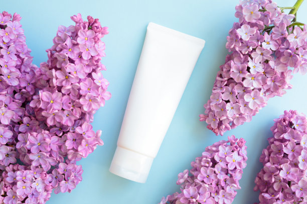 模拟白色挤压瓶化妆品管和丁香花在蓝色的背景。面霜、润滑凝胶、保湿霜、护肤品、防晒霜。平铺，正面视图，空白管，模板。图片下载