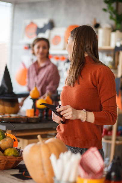 年轻女子在制作万圣节装饰品时，扭头微笑着看着她的母亲图片下载