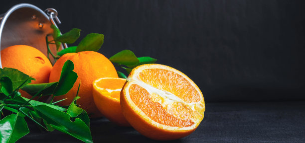 很多新鲜的橙子水果放在不锈钢篮子里，倒在黑色的木质背景上。图片下载