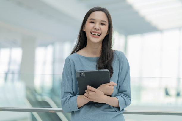 亚洲微笑开朗女性数码游牧民手持平板设备看相机人像拍摄，幸福微笑的亚洲女性站在办公室学院走廊积极微笑的态度图片下载