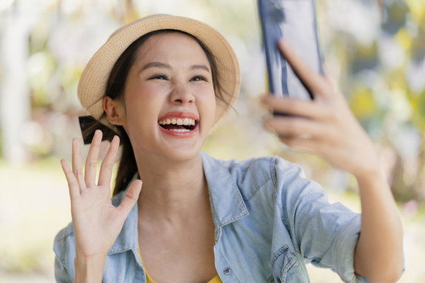 说嗨手势问候视频打电话给家人国外连接，亚洲女性数字游牧民用智能手机打电话说嗨她的家人或朋友，而度假旅行在海滩工作的任何地方图片下载