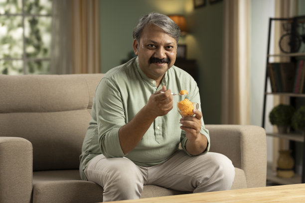 成熟男人坐在沙发上吃冰淇淋的照片图片下载