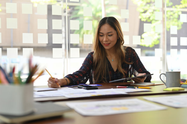 泰国亚洲女性工作在她的设计开发人员的职业生涯，同时在纸上写东西与专注的脸在现代办公室内部。创新的数字化发展理念。图片下载