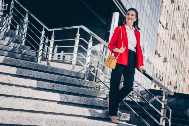 梦幻可爱的成熟女性领导人穿着红色夹克在城市商业大楼外微笑着走楼梯的照片图片下载