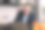 一个年轻的成功商人的肖像使用笔记本电脑坐在家里的厨房里，穿着商务西装，戴着眼镜。一名男子微笑着看着水果篮旁的笔记本电脑显示器图片下载