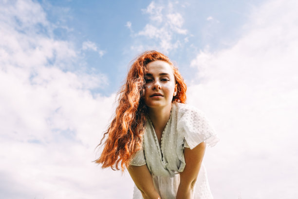 年轻的姜微笑的女人在天空的背景。图片下载