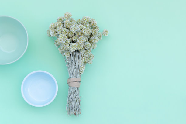 俯瞰绿色和蓝色陶瓷碗和花束干蜡菊花在绿色薄荷背景。副本的空间。平面构成。图片下载