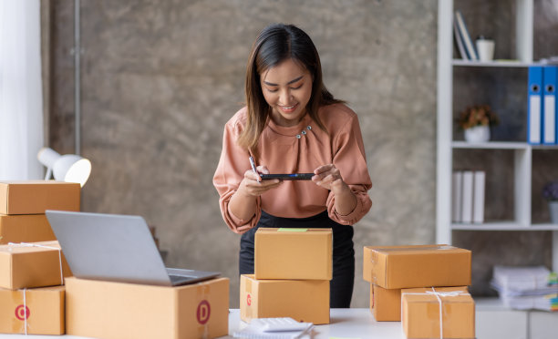 年轻的亚洲女性用手机或智能手机数码相机拍下邮箱地址的照片，在网上出售，并准备包装产品包装盒。销售中小企业网上想法概念图片下载