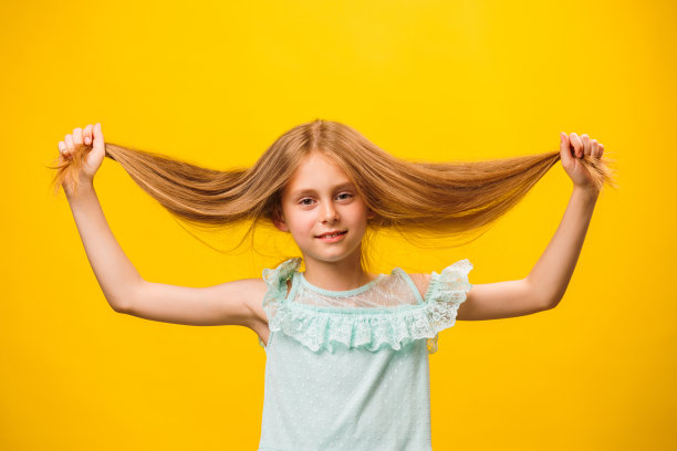女孩站在黄色的背景上。用手抓头发。图片下载