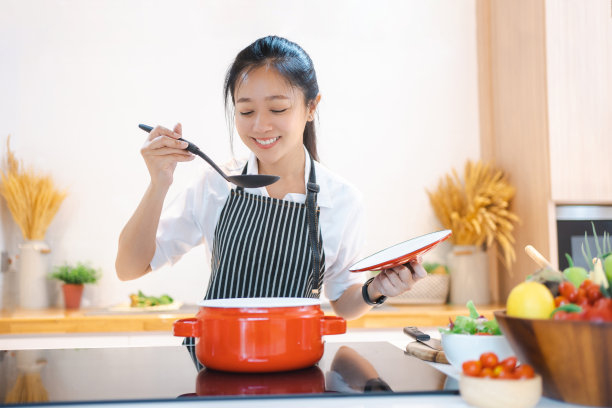 快乐微笑的亚洲妇女在围裙品尝和闻到食物，而在厨房做饭。图片下载