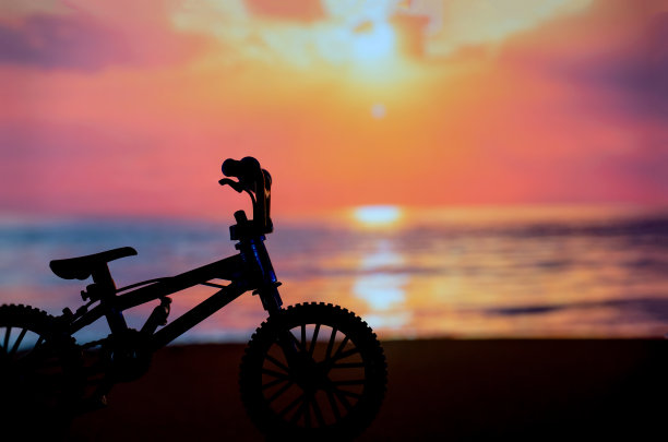沙滩上的自行车剪影照片，以夕阳黄昏时刻为背景图片下载
