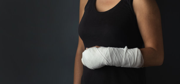 一个在深灰色背景上胳膊上打了石膏的女人。女孩有一只受伤的手，穿着黑色t恤图片下载