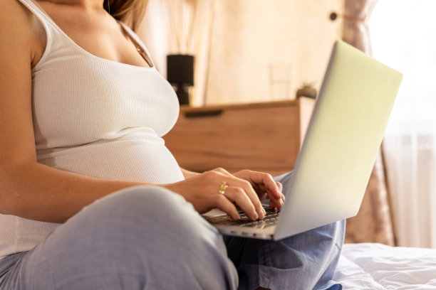 女人抱着电脑。移动孕期上网孕妇笔记本申请。孕妇使用数码笔记本电脑。怀孕、医药、制药、保健和人的概念。图片下载