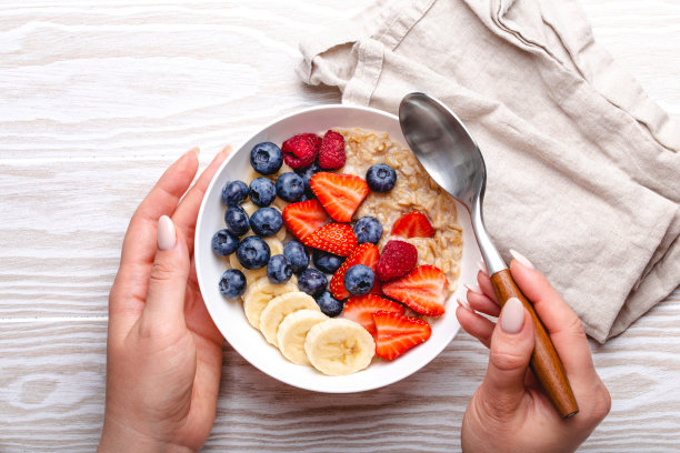 俯视图的女性手拿着碗燕麦粥水果和浆果图片下载