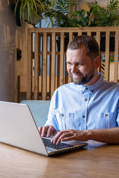 微笑的年轻人在咖啡店使用小工具。满脸笑容的大胡子帅哥正在用笔记本电脑看邮件图片下载
