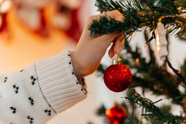 一个穿着新年毛衣的女孩的手在圣诞树上挂着一个球。图片下载