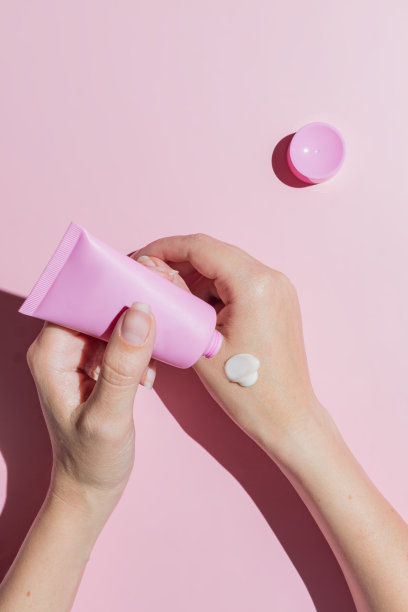 女性手使用化妆品皮肤护理润肤霜在皮肤上的粉红色的背景。为设计师设计的化妆品模型图片下载