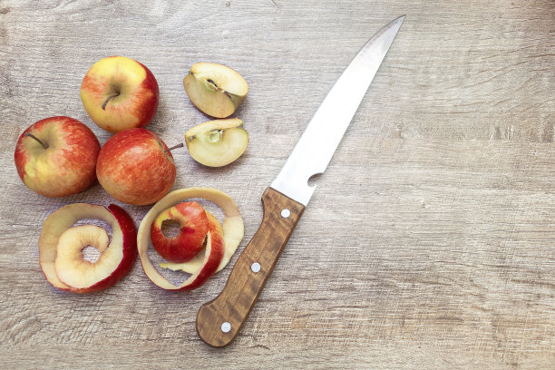 把成熟的苹果切成红色，用刀在木桌上削皮。新鲜水果的背景与文字复制空间，烹饪概念图片下载