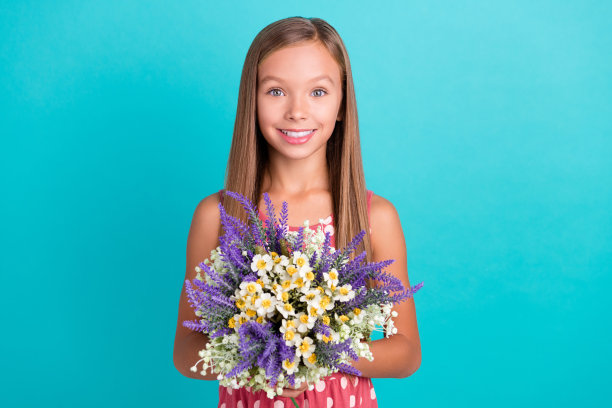 照片中迷人可爱的小女孩穿着粉色连衣裙，捧着绿松石色背景的花束图片下载