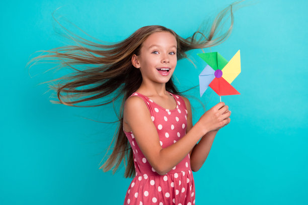 可爱时髦的小女孩穿粉红色的裙子微笑着抱着纺纱风吹孤立的蓝绿色背景照片图片下载