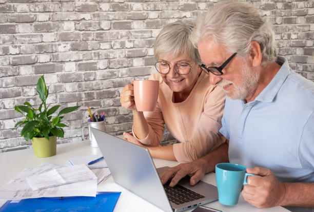 现代高级夫妇微笑着浏览笔记本电脑，喝一杯咖啡或茶。图片下载