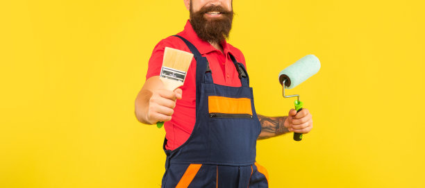 裁剪快乐的人在工作服装装饰举行油漆辊和刷黄色的背景图片下载