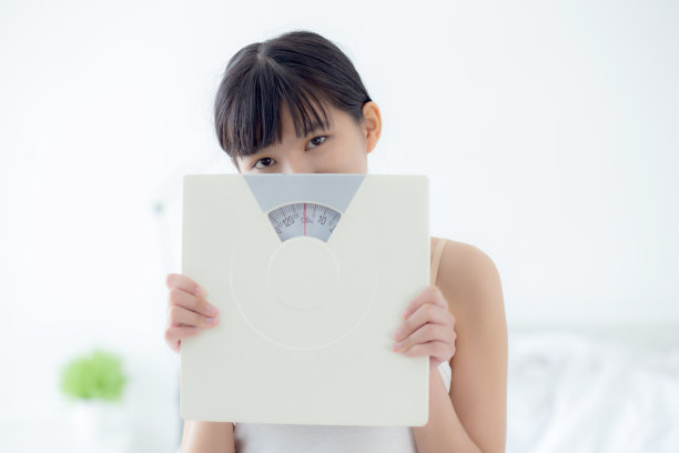 年轻美丽的亚洲女性手持秤与自信的控制和减肥，女孩节食减肥的结果与满意，一个人，健康的生活方式的概念。图片下载