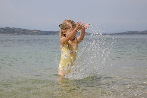 可爱的蹒跚学步的女孩穿着黄色泳衣在海滩上泼水。田园式的暑假概念。图片下载