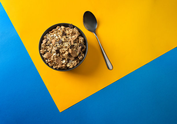 什锦麦片碗与奇亚，藜麦，坚果，种子，巧克力片和勺子在黄蓝色的背景。前视图。图片下载