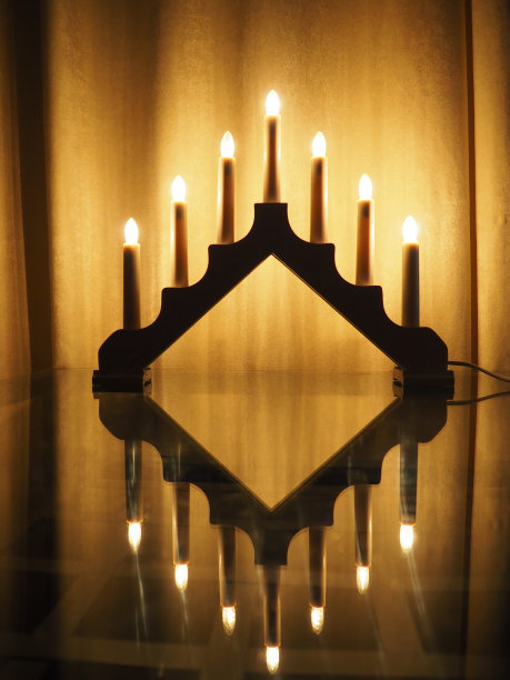 Schwibbogen拱门灯具，玻璃桌上的三角形烛台。黄色背景。晚上，有浪漫、喜庆、宗教或神秘的气氛。燃烧着像烛光一样的灯泡。图片下载