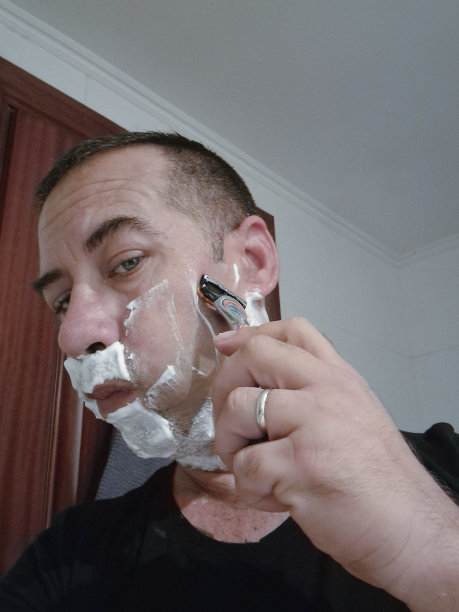 一个年轻人满脸都是剃须泡沫，在浴室里剃须图片下载