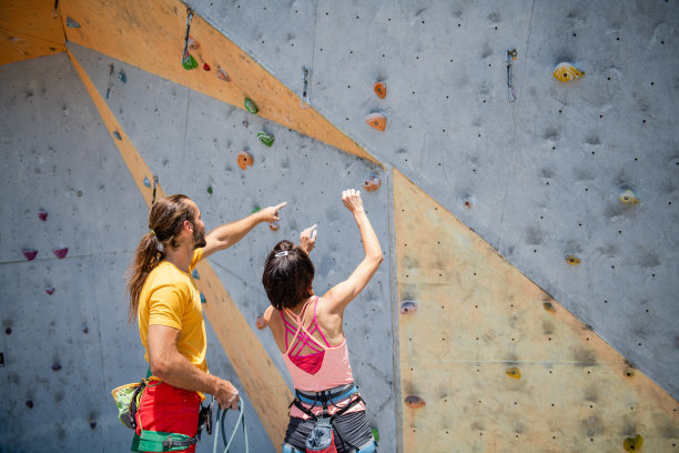 一名女子攀岩者和一名男子教练在攀岩墙的背景上图片下载