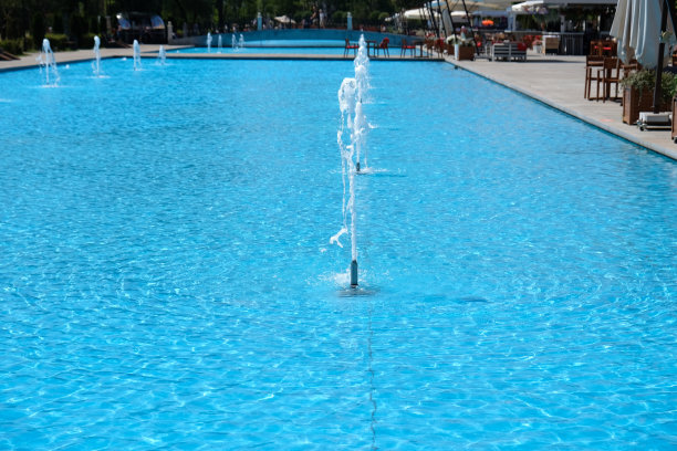 垂直水流的喷泉，碧蓝的水。溪流从管子里流出。夏季的城市。选择软焦点。模糊的咖啡馆或酒吧背景。现代喷泉中的一排喷水。图片下载