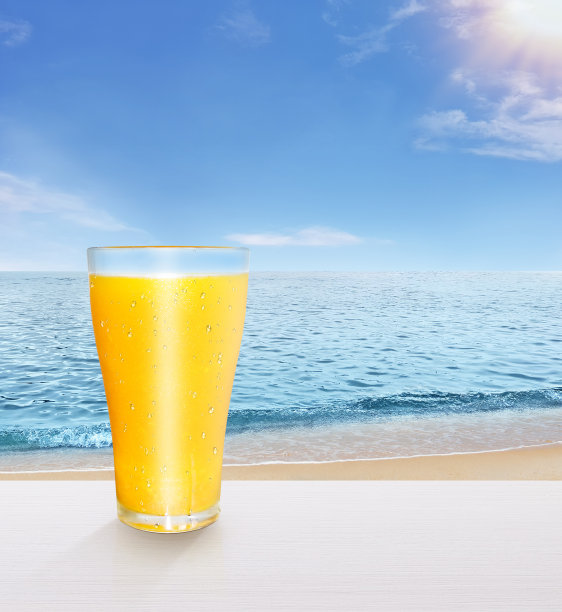 橙汁装在玻璃杯里，健康放在白色木桌上。以天空和大海为背景图片下载