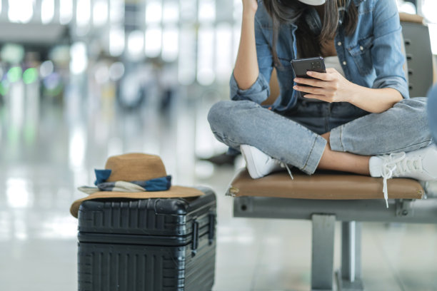 迷人的亚洲女性旅行者戴着卡苏拉布耳机使用笔记本电脑在机场候机楼等待航班起飞，亚洲女性微笑挥手问候看着相机旅行的想法概念图片下载