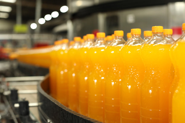 生产碳酸饮料。橙色的瓶子在生产线上。图片下载