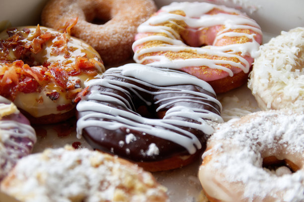 什锦甜甜圈装在盒子里的图片，上面有糖霜巧克力、粉巧克力和巧克力屑甜甜圈。图片下载