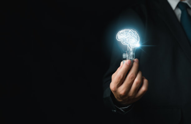 一个富有创造力的商人穿着西装，拿着一个头脑明亮的灯泡来构思新事物。图片下载