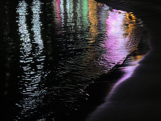 夜晚的海浪在沙滩上与五颜六色的霓虹灯反射。图片下载