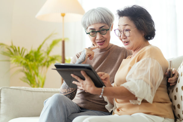 拜访两位年长的成熟女性朋友的房子通过老照片，数码相册一起平板设备在客厅的沙发在家里老朋友一起度过优质的时间图片下载