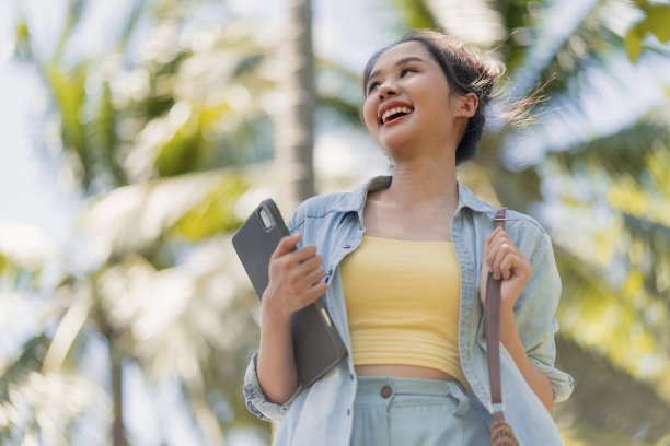 放松休闲，无忧无虑，微笑的亚洲女性数字游牧民自由编程手拿笔记本走在海滩和椰子树蓝天，新千禧一代的生活方式，工作在任何地方与幸福图片下载