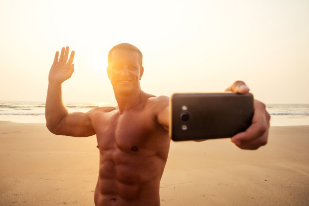 英俊成功的男性运动员健身模型拍摄自拍肖像电话海滩天堂日落。在热带度假的男人用智能手机与朋友和家人在线聊天图片下载